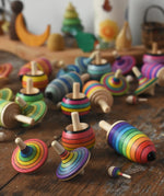 Mader Kreiselmanufaktur rainbow spinning top learning set placed on a wooden surface in the Babipur playroom. Other colour variations of the same set can be seen in the background.