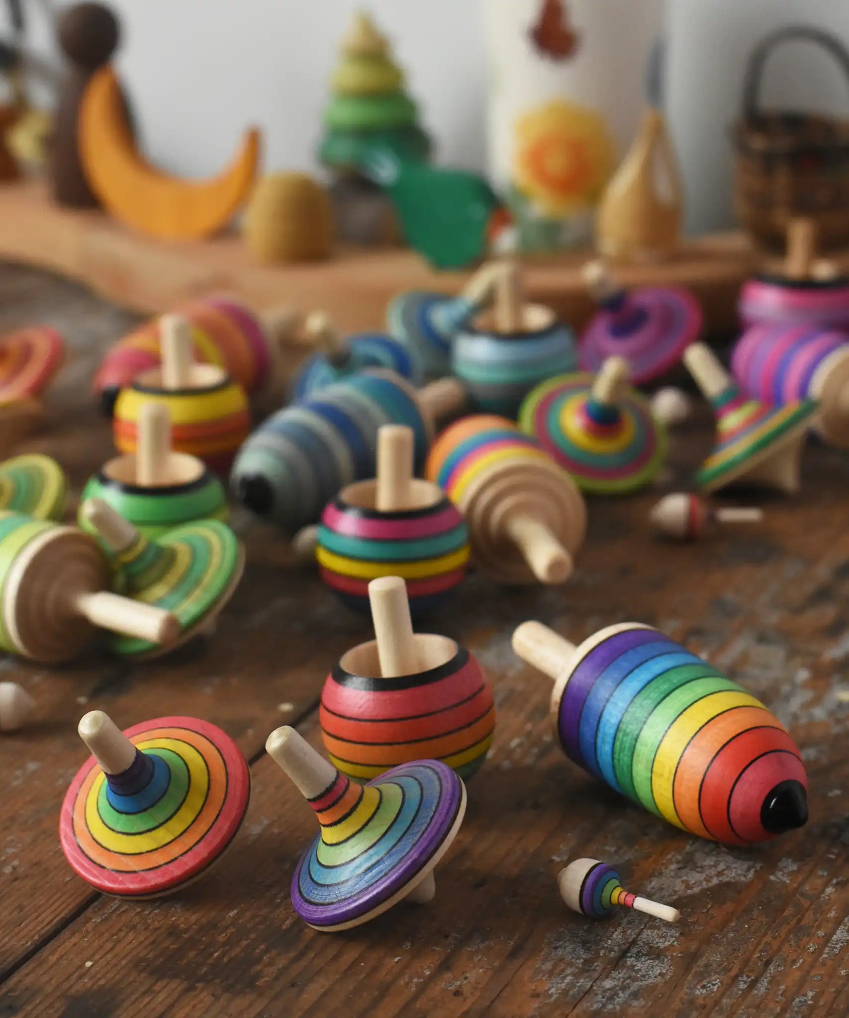 Mader Kreiselmanufaktur rainbow spinning top learning set placed on a wooden surface in the Babipur playroom. Other colour variations of the same set can be seen in the background.
