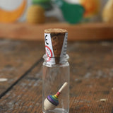 The miniature spinning top from the Mader Kreiselmanufaktur rainbow spinning top learning set inside it's glass, cork top jar placed on a wooden surface in the Babipur playroom. 