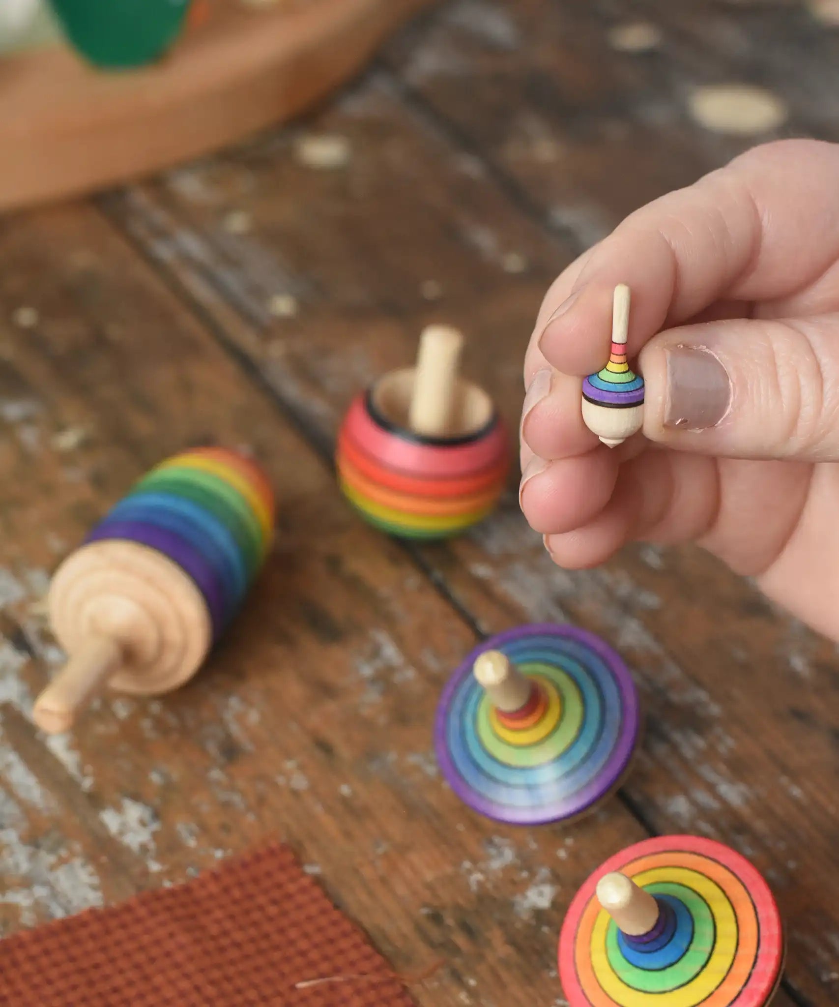 The miniature Mader Kreiselmanufaktur rainbow spinning top from the rainbow spinning top learning set in an adult's hand in the Babipur playroom. 