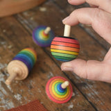 Mader Kreiselmanufaktur rainbow turnover top  from the rainbow spinning top learning set in an adult's hand in the Babipur playroom.