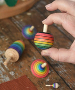 Mader Kreiselmanufaktur rainbow turnover top  from the rainbow spinning top learning set in an adult's hand in the Babipur playroom.