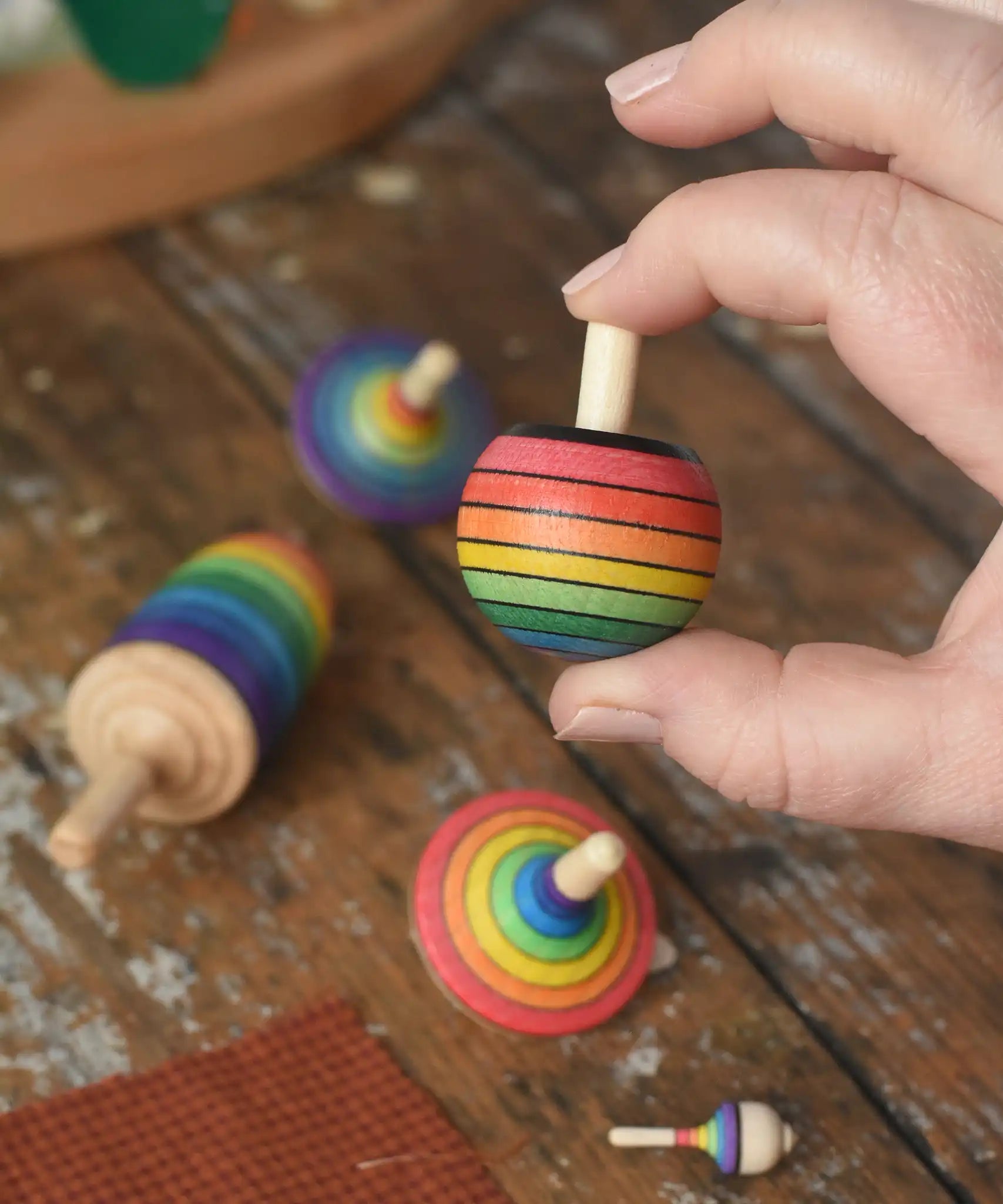 Mader Kreiselmanufaktur rainbow turnover top  from the rainbow spinning top learning set in an adult's hand in the Babipur playroom.