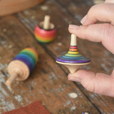 Rainbow spinning top from the Mader Kreiselmanufaktur rainbow spinning top learning set in an adult's hand in the Babipur playroom. 