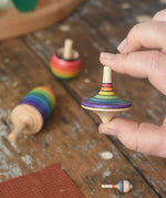 Rainbow spinning top from the Mader Kreiselmanufaktur rainbow spinning top learning set in an adult's hand in the Babipur playroom. 