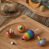 Mader Kreiselmanufaktur rainbow spinning top learning set placed on an oak spinning plate on a wooden surface in the Babipur playroom. 