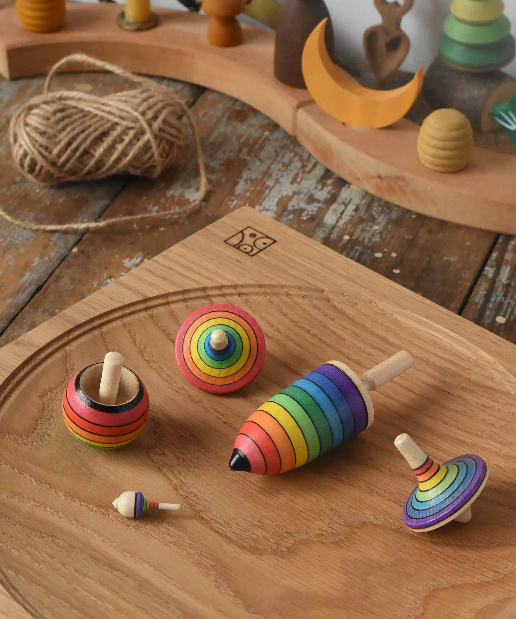 Mader Kreiselmanufaktur rainbow spinning top learning set placed on an oak spinning plate on a wooden surface in the Babipur playroom. 