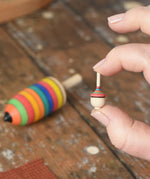 Miniature spinner from the Mader Kreiselmanufaktur striped spinning top learning set in an adult's hand in the Babipur playroom. 