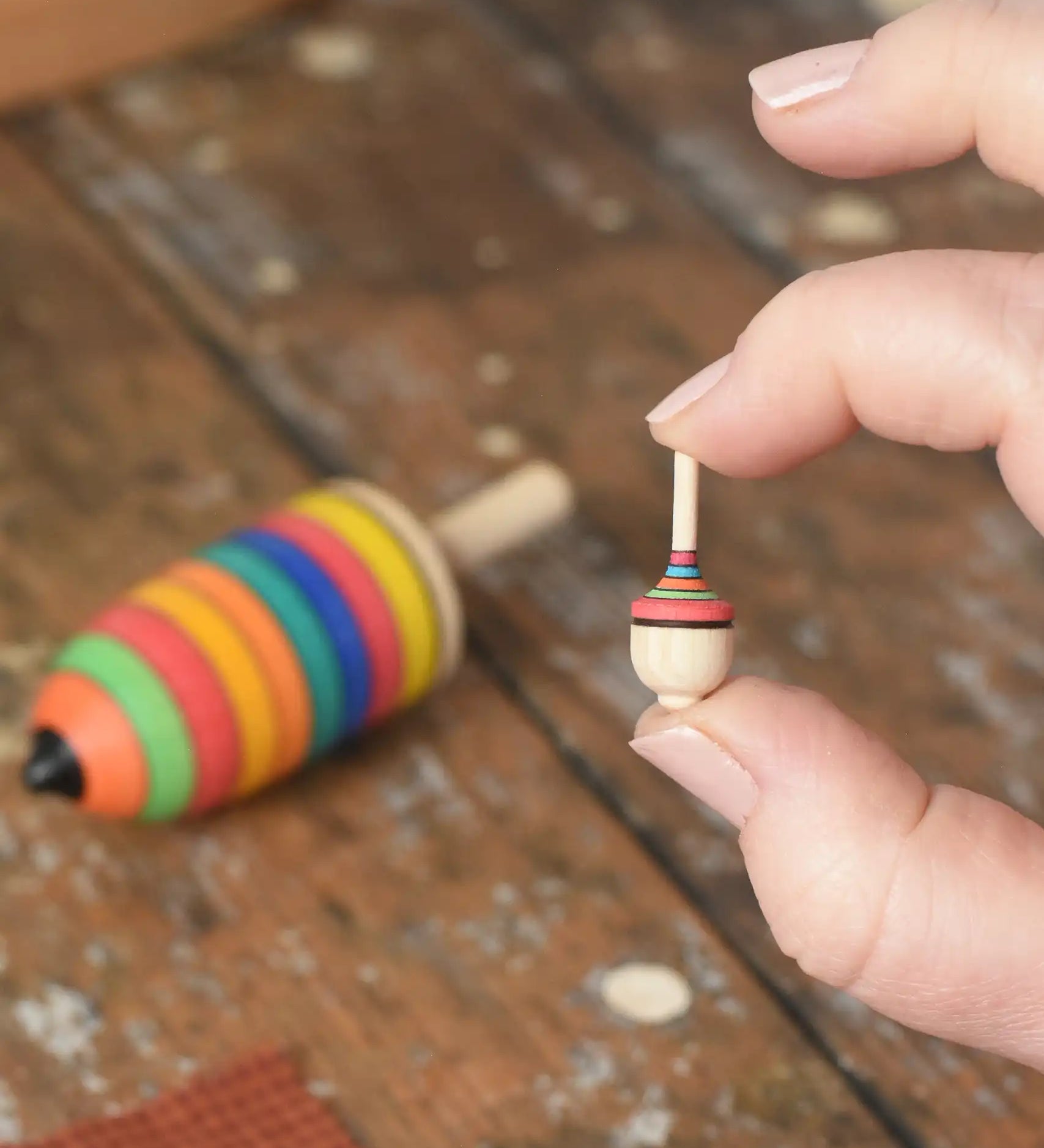Miniature spinner from the Mader Kreiselmanufaktur striped spinning top learning set in an adult's hand in the Babipur playroom. 