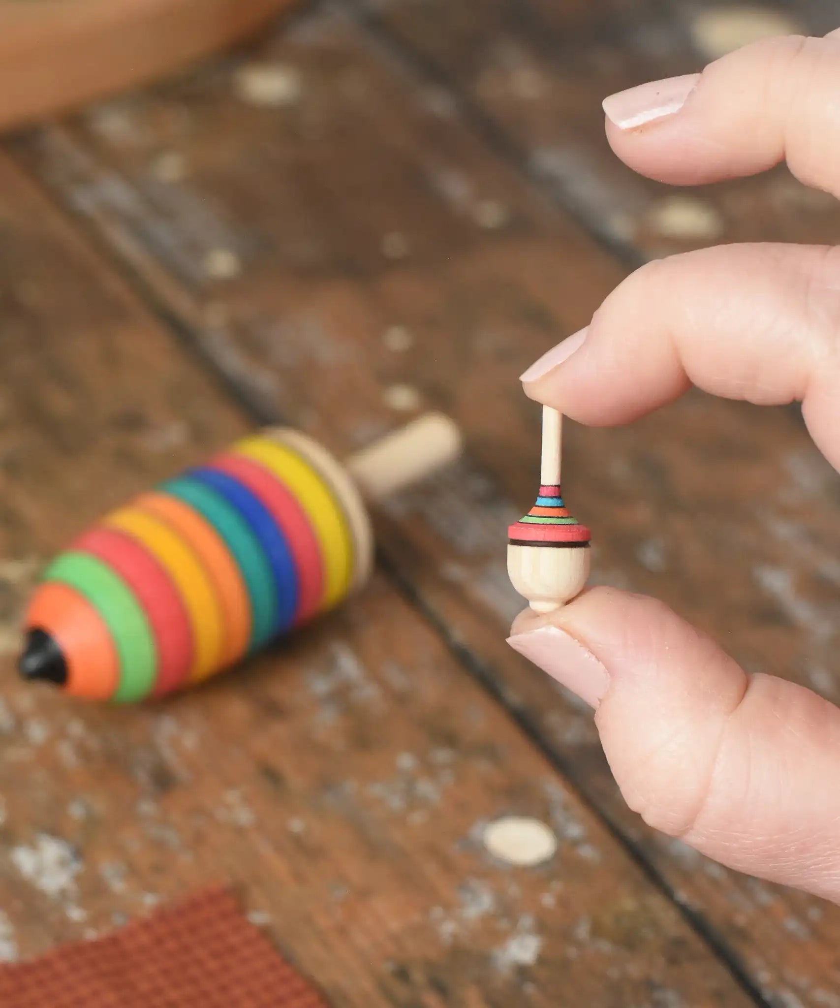 Miniature spinner from the Mader Kreiselmanufaktur striped spinning top learning set in an adult's hand in the Babipur playroom. 