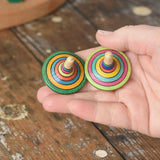Two rallye spinners from the Mader Kreiselmanufaktur striped spinning top learning set in an adult's hand in the Babipur playroom. 