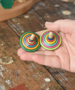 Two rallye spinners from the Mader Kreiselmanufaktur striped spinning top learning set in an adult's hand in the Babipur playroom. 