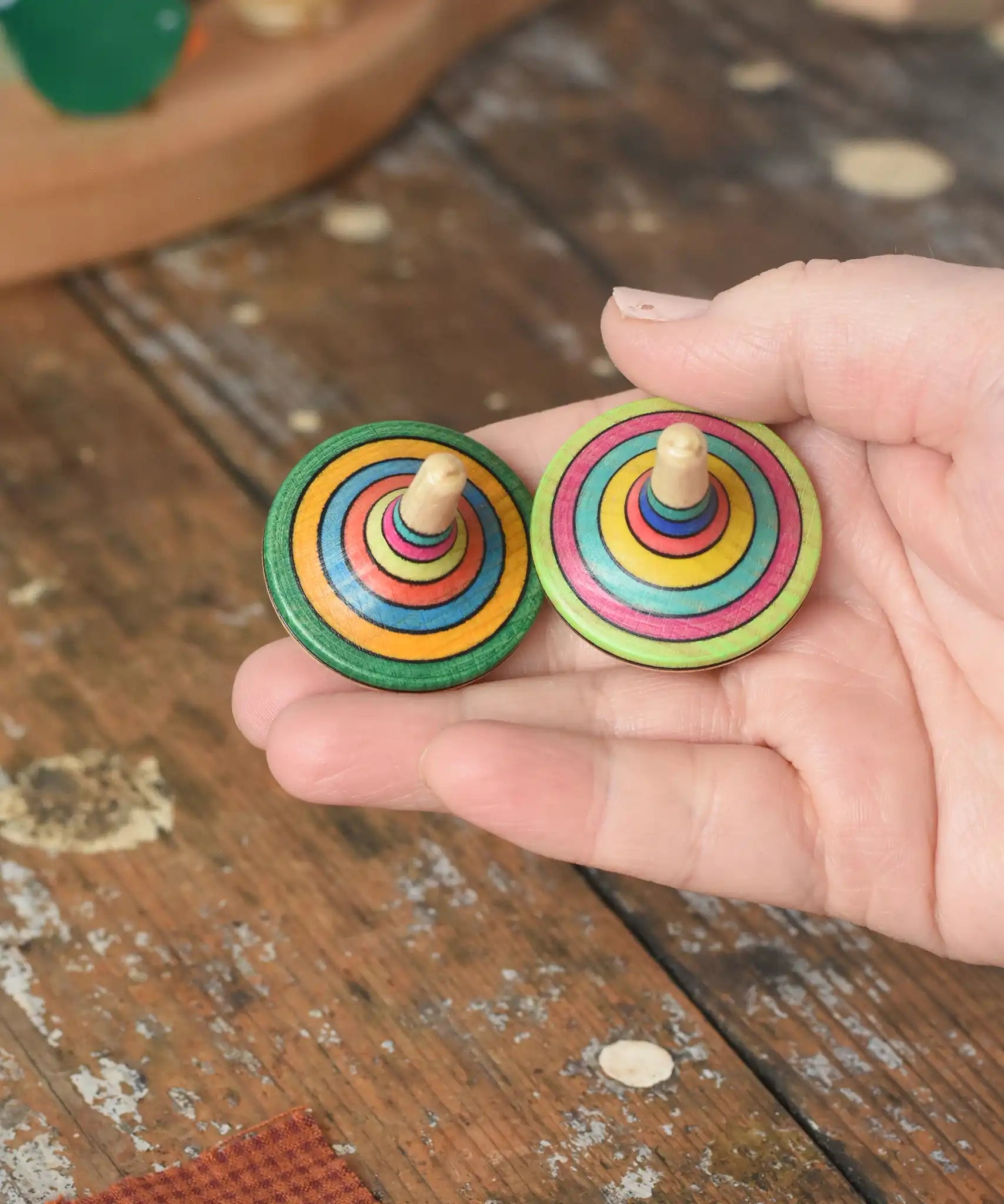Two rallye spinners from the Mader Kreiselmanufaktur striped spinning top learning set in an adult's hand in the Babipur playroom. 