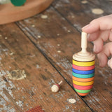 The thunderbolt and mini spinners from the Mader Kreiselmanufaktur striped spinning top learning set placed on a wooden surface in the Babipur playroom. An adult's hand can be seen holding up the thunderbolt.