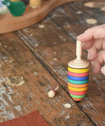 The thunderbolt and mini spinners from the Mader Kreiselmanufaktur striped spinning top learning set placed on a wooden surface in the Babipur playroom. An adult's hand can be seen holding up the thunderbolt.