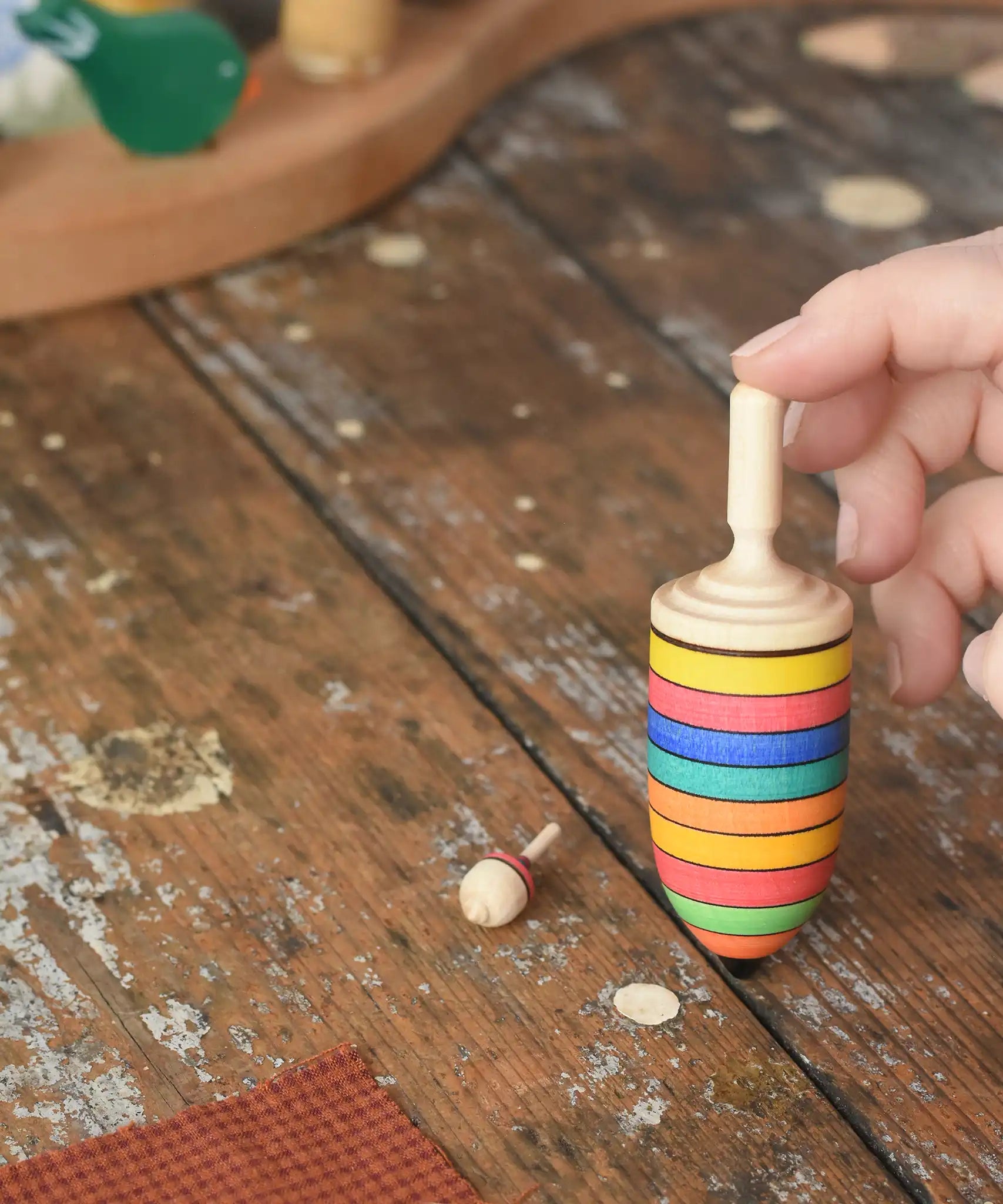 The thunderbolt and mini spinners from the Mader Kreiselmanufaktur striped spinning top learning set placed on a wooden surface in the Babipur playroom. An adult's hand can be seen holding up the thunderbolt.