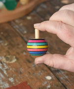 Turnover spinning top from the Mader Kreiselmanufaktur striped spinning top learning set in an adult's hand in the Babipur playroom. 