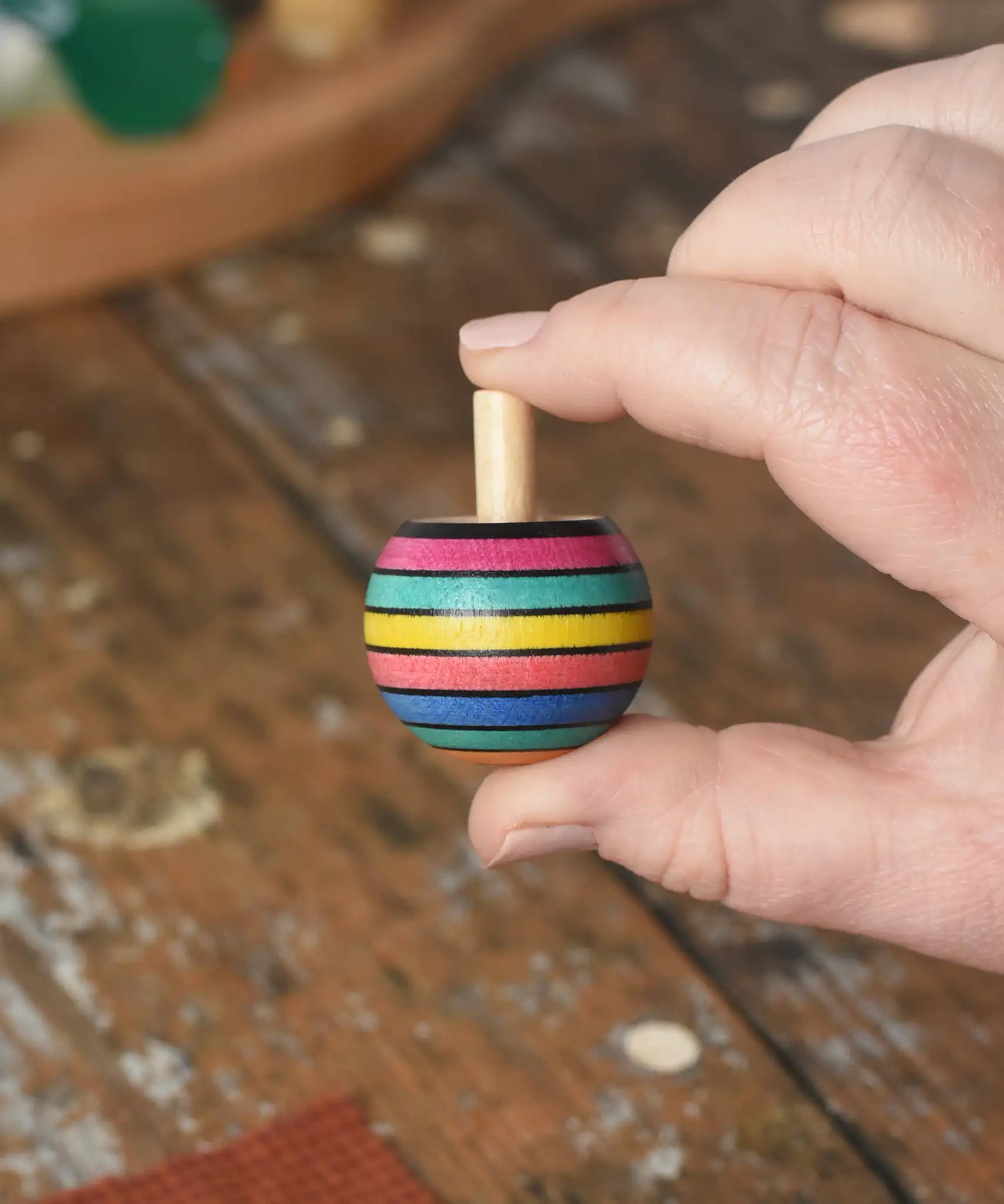 Turnover spinning top from the Mader Kreiselmanufaktur striped spinning top learning set in an adult's hand in the Babipur playroom. 