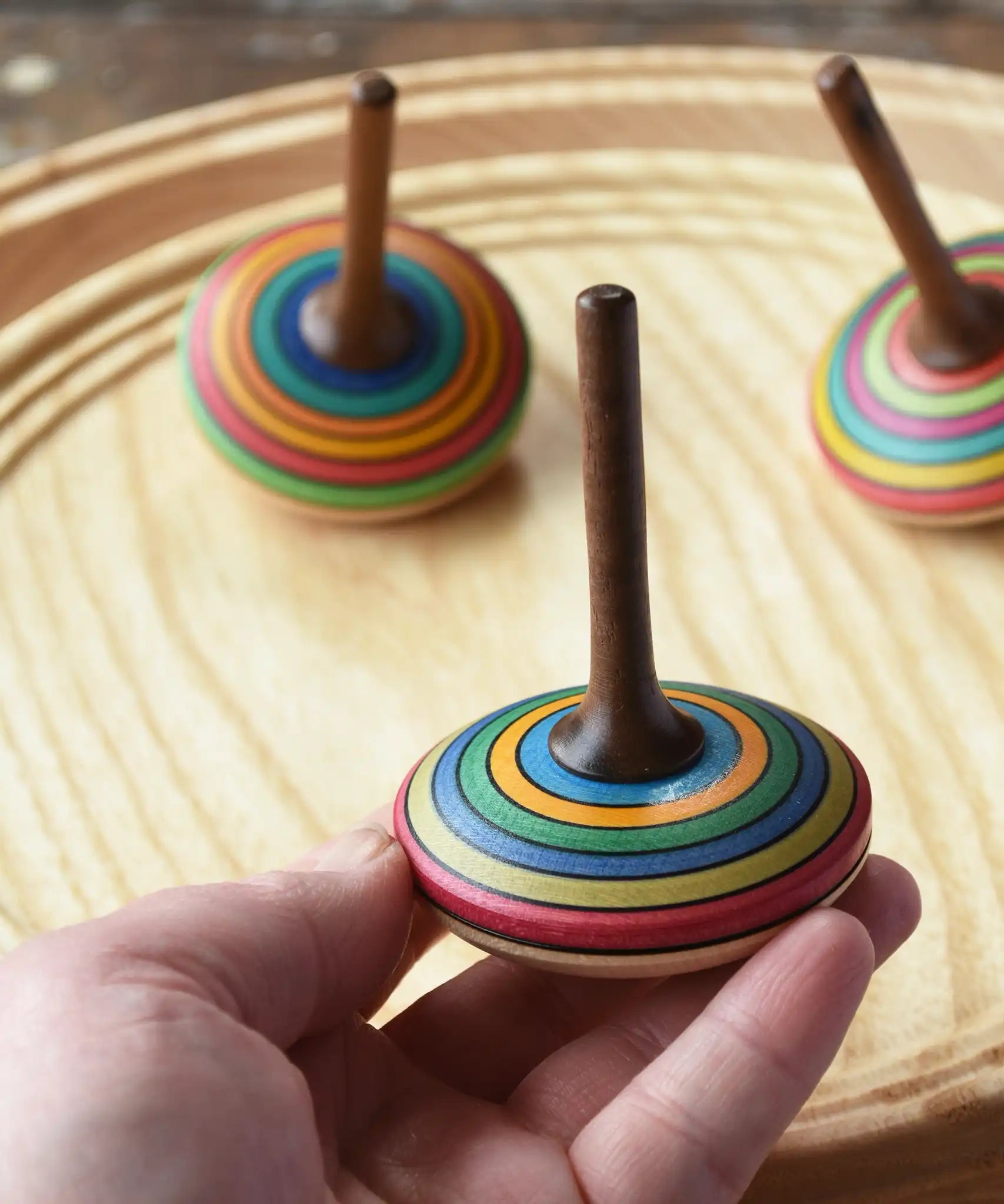 Mader stripe spinning tops placed on a spinning plate with one in an adult's hand. 