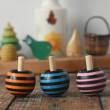 Three Mader tango turn-over spinning tops placed on a wooden desk in the Babipur playroom. 