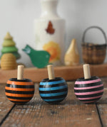 Three Mader tango turn-over spinning tops placed on a wooden desk in the Babipur playroom. 