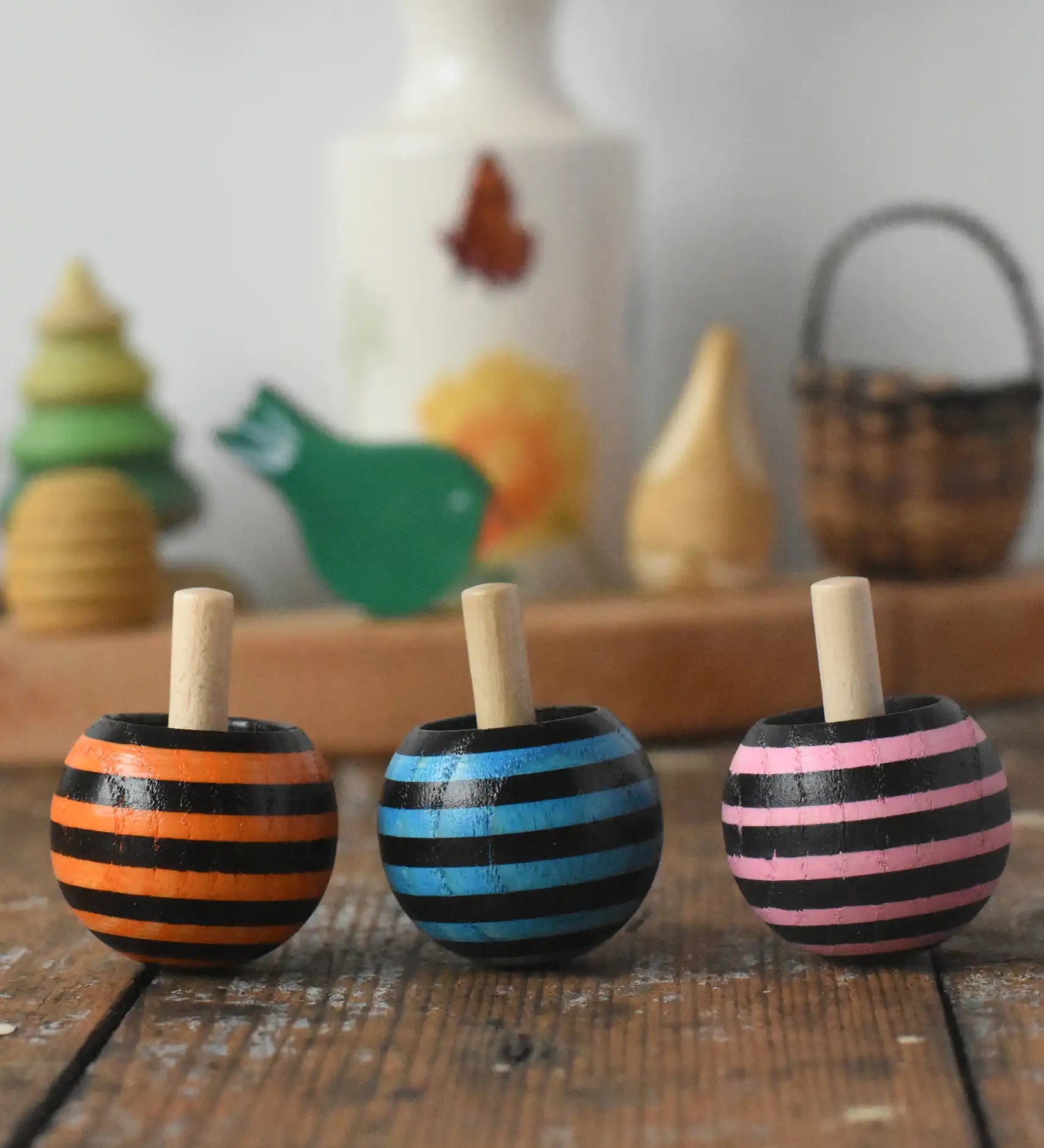 Three Mader tango turn-over spinning tops placed on a wooden desk in the Babipur playroom. 