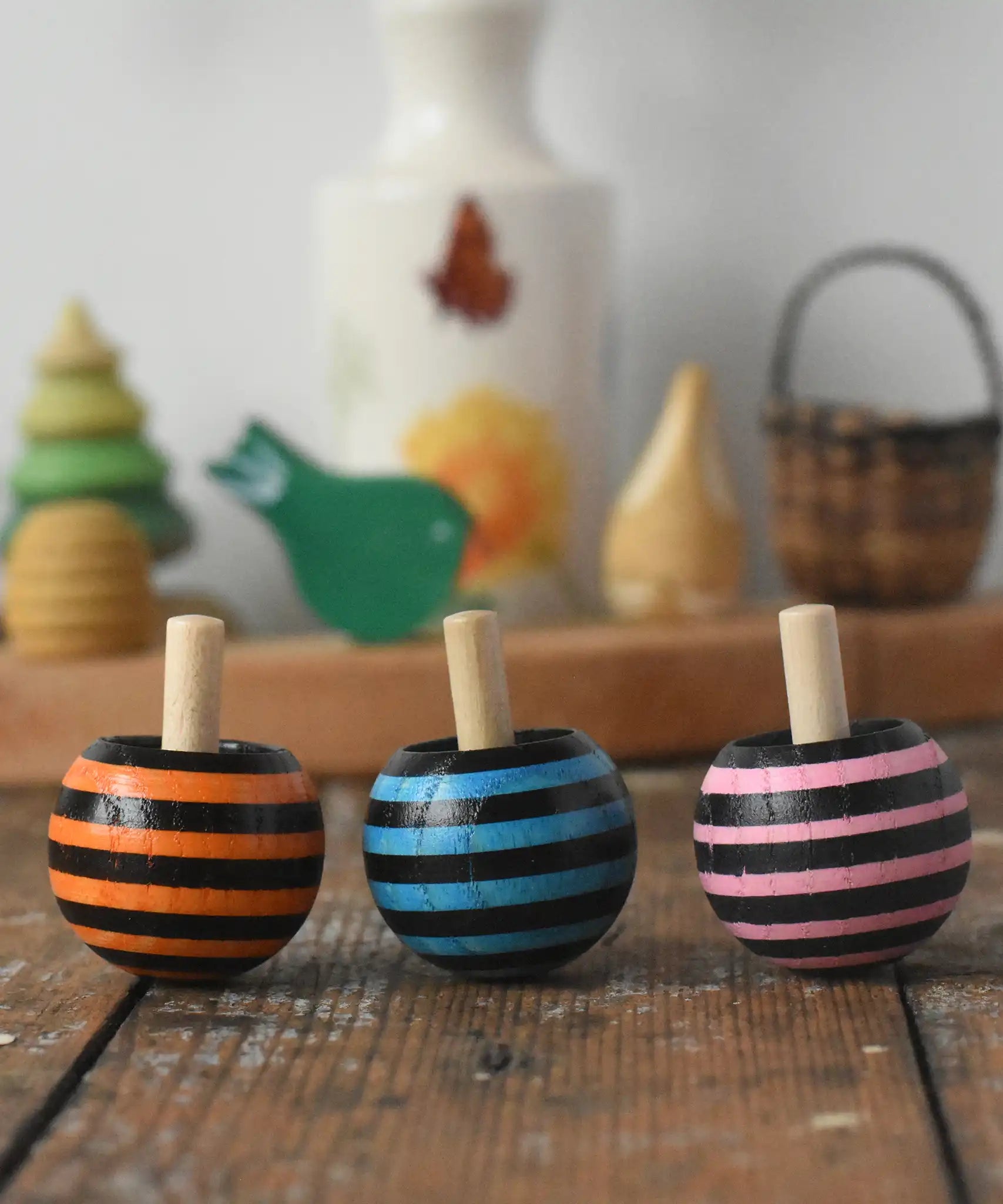 Three Mader tango turn-over spinning tops placed on a wooden desk in the Babipur playroom. 