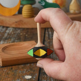 Mader Kreiselmanufaktur superstar wooden spinning top toy shown in an adult's hand with and spinning plate placed on a wooden desk in the Babipur playroom.