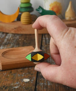 Mader Kreiselmanufaktur superstar wooden spinning top toy shown in an adult's hand with and spinning plate placed on a wooden desk in the Babipur playroom.