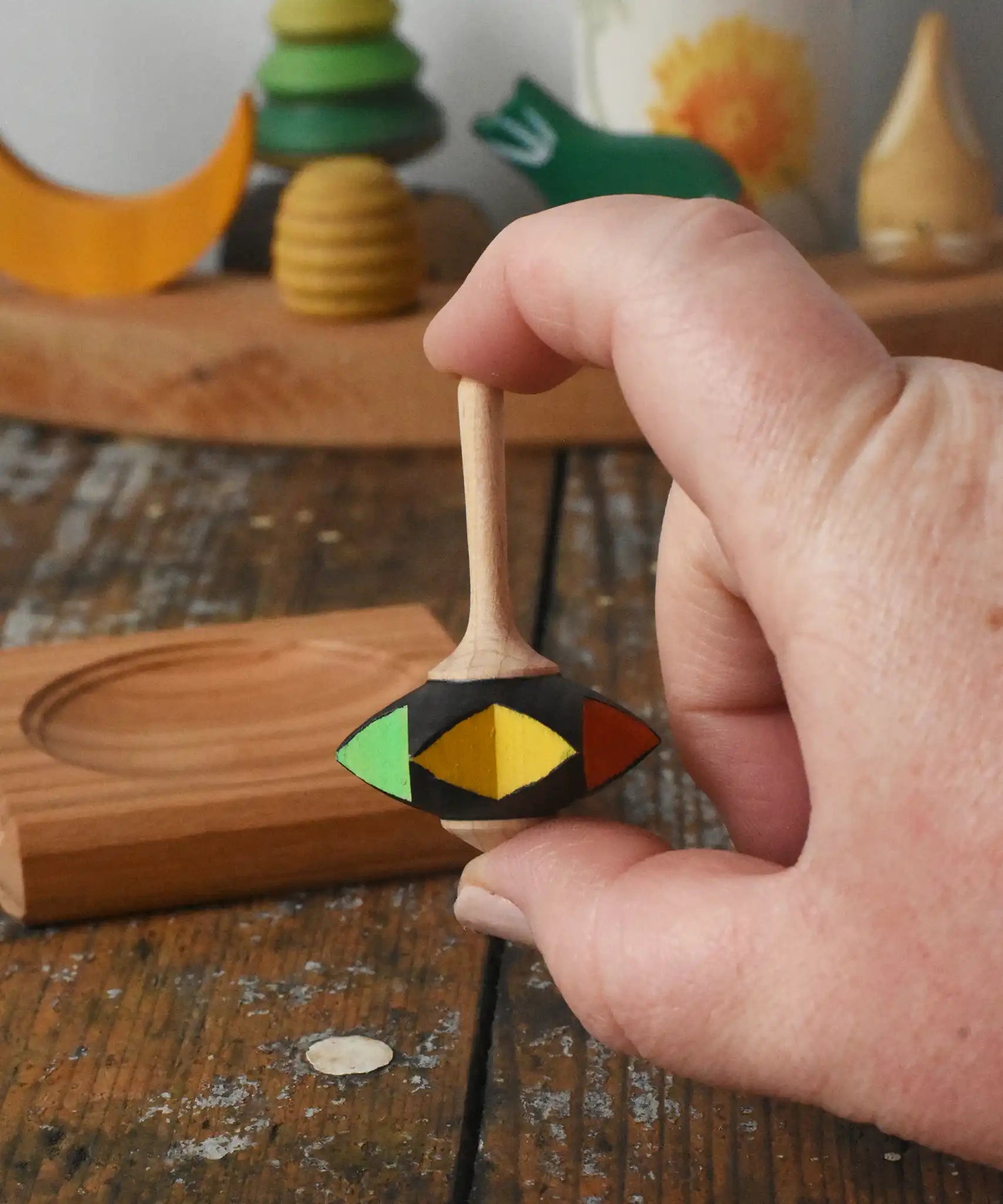 Mader Kreiselmanufaktur superstar wooden spinning top toy shown in an adult's hand with and spinning plate placed on a wooden desk in the Babipur playroom.