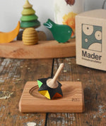 Mader Kreiselmanufaktur superstar wooden spinning top toy with and spinning plate placed on a wooden desk in the Babipur playroom.