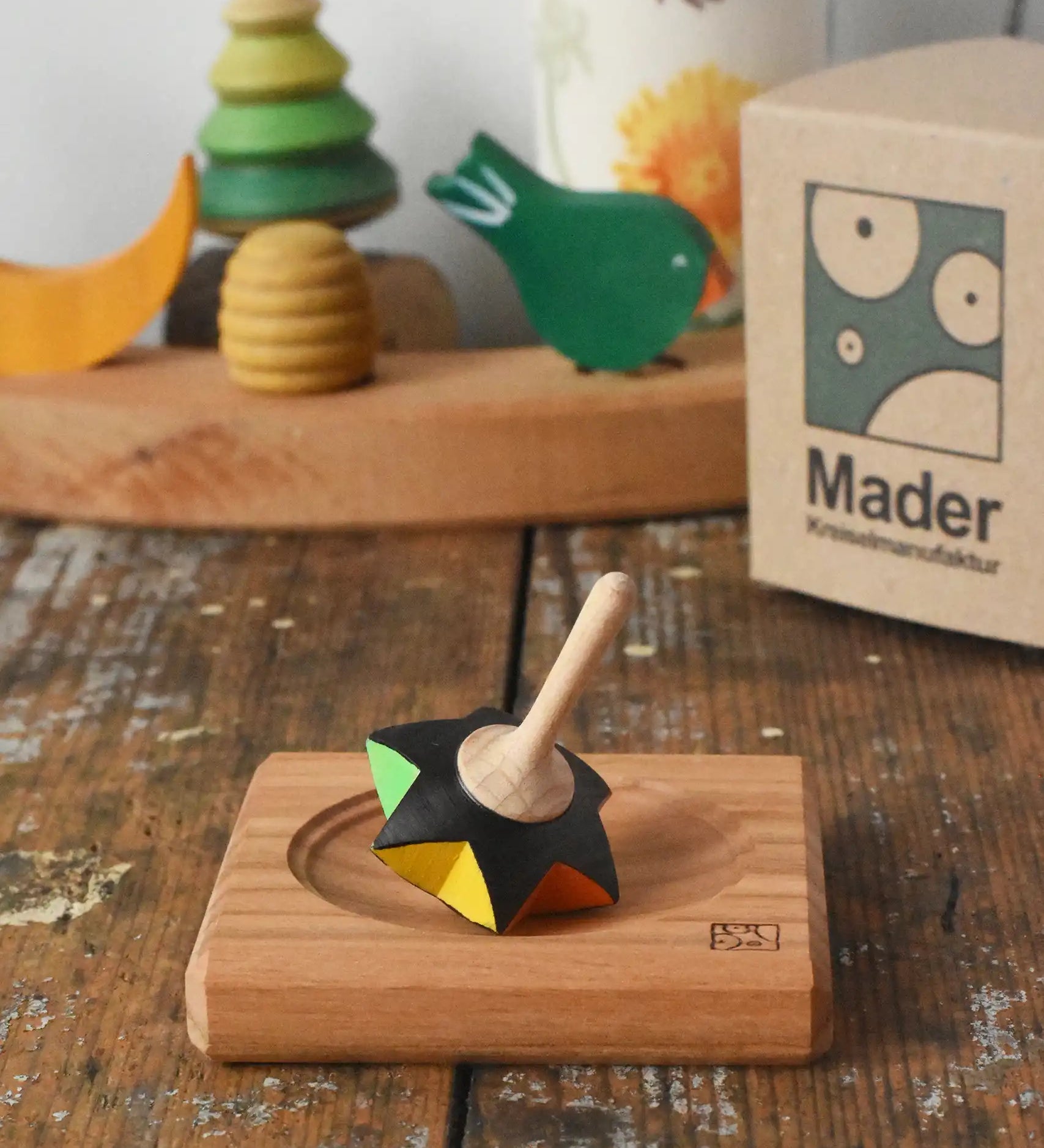 Mader Kreiselmanufaktur superstar wooden spinning top toy with and spinning plate placed on a wooden desk in the Babipur playroom.