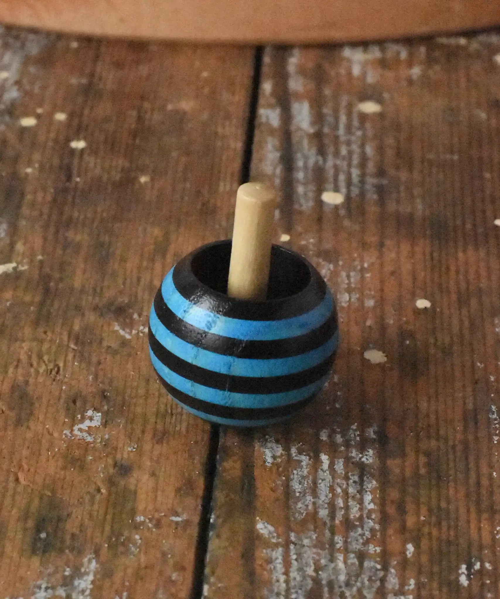 Blue striped Mader tango turn-over spinning top placed on a wooden desk in the Babipur playroom. 