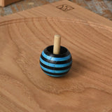 Blue Mader tango turn-over spinning top placed on an oak spinning plate on a wooden desk in the Babipur playroom. 
