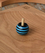 Blue Mader tango turn-over spinning top placed on an oak spinning plate on a wooden desk in the Babipur playroom. 