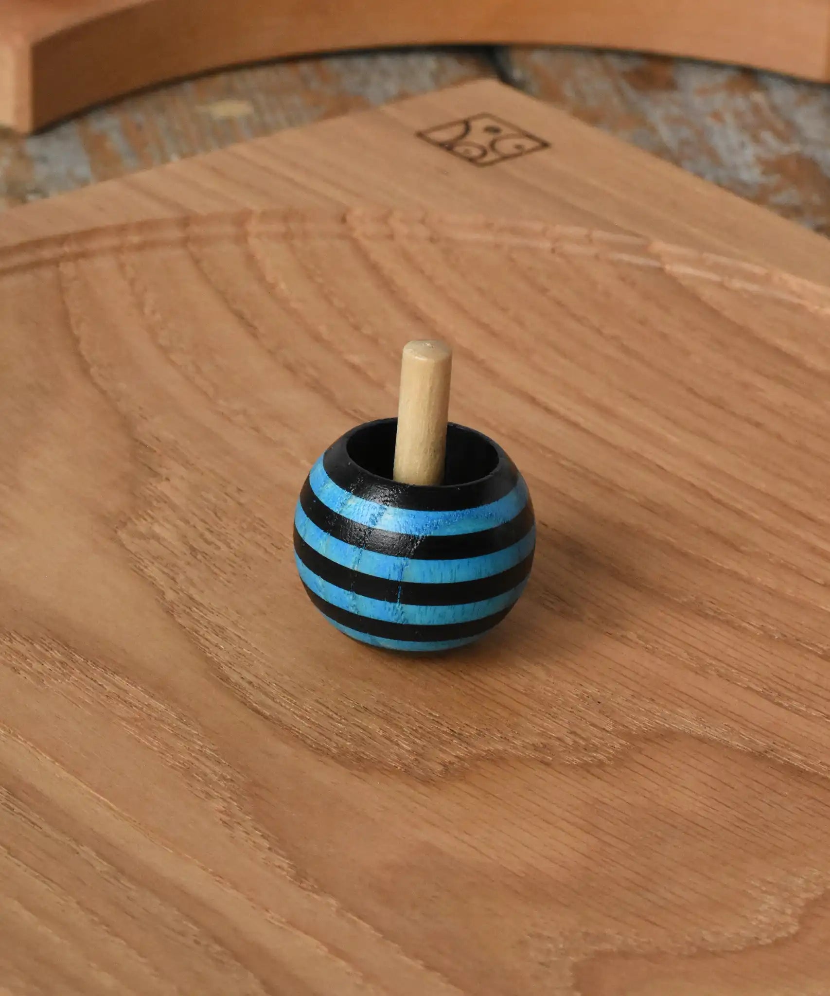 Blue Mader tango turn-over spinning top placed on an oak spinning plate on a wooden desk in the Babipur playroom. 