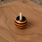 Orange Mader tango turn-over spinning top placed on an oak spinning plate on a wooden desk in the Babipur playroom. 