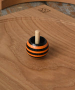 Orange Mader tango turn-over spinning top placed on an oak spinning plate on a wooden desk in the Babipur playroom. 