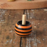 Orange striped Mader tango turn-over spinning top placed on a wooden desk in the Babipur playroom. 