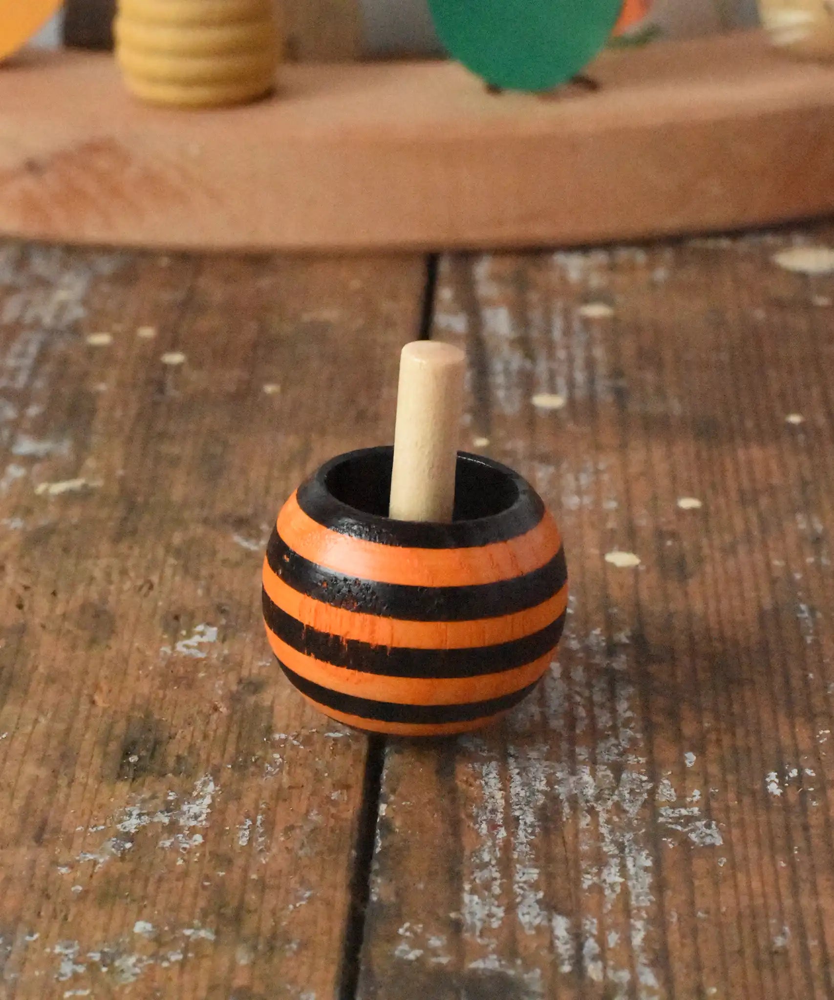 Orange striped Mader tango turn-over spinning top placed on a wooden desk in the Babipur playroom. 