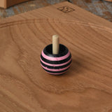 Pink Mader tango turn-over spinning top placed on an oak spinning plate on a wooden desk in the Babipur playroom. 