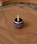 Pink Mader tango turn-over spinning top placed on an oak spinning plate on a wooden desk in the Babipur playroom. 