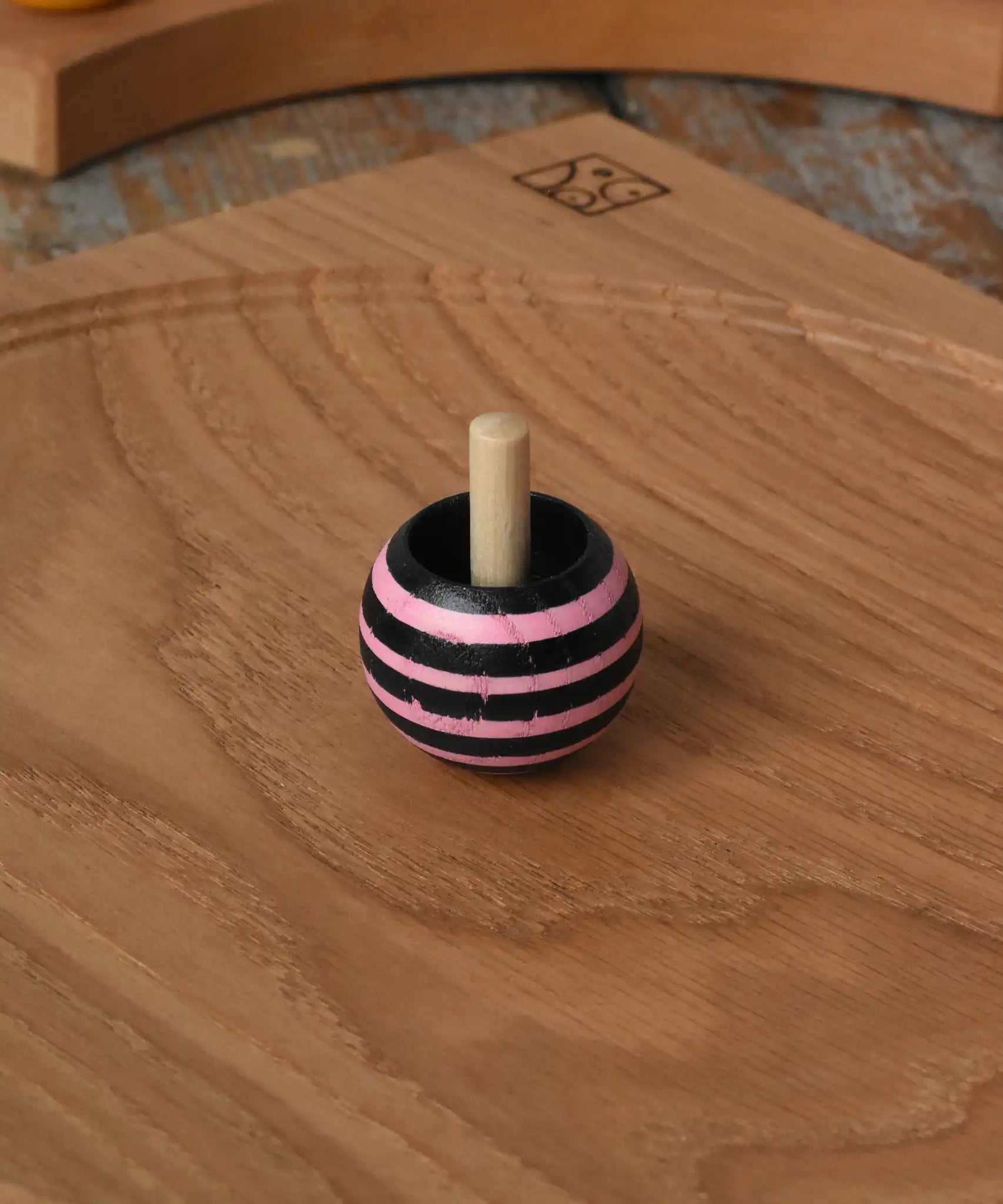 Pink Mader tango turn-over spinning top placed on an oak spinning plate on a wooden desk in the Babipur playroom. 