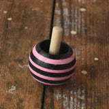 Pink striped Mader tango turn-over spinning top placed on a wooden desk in the Babipur playroom. 