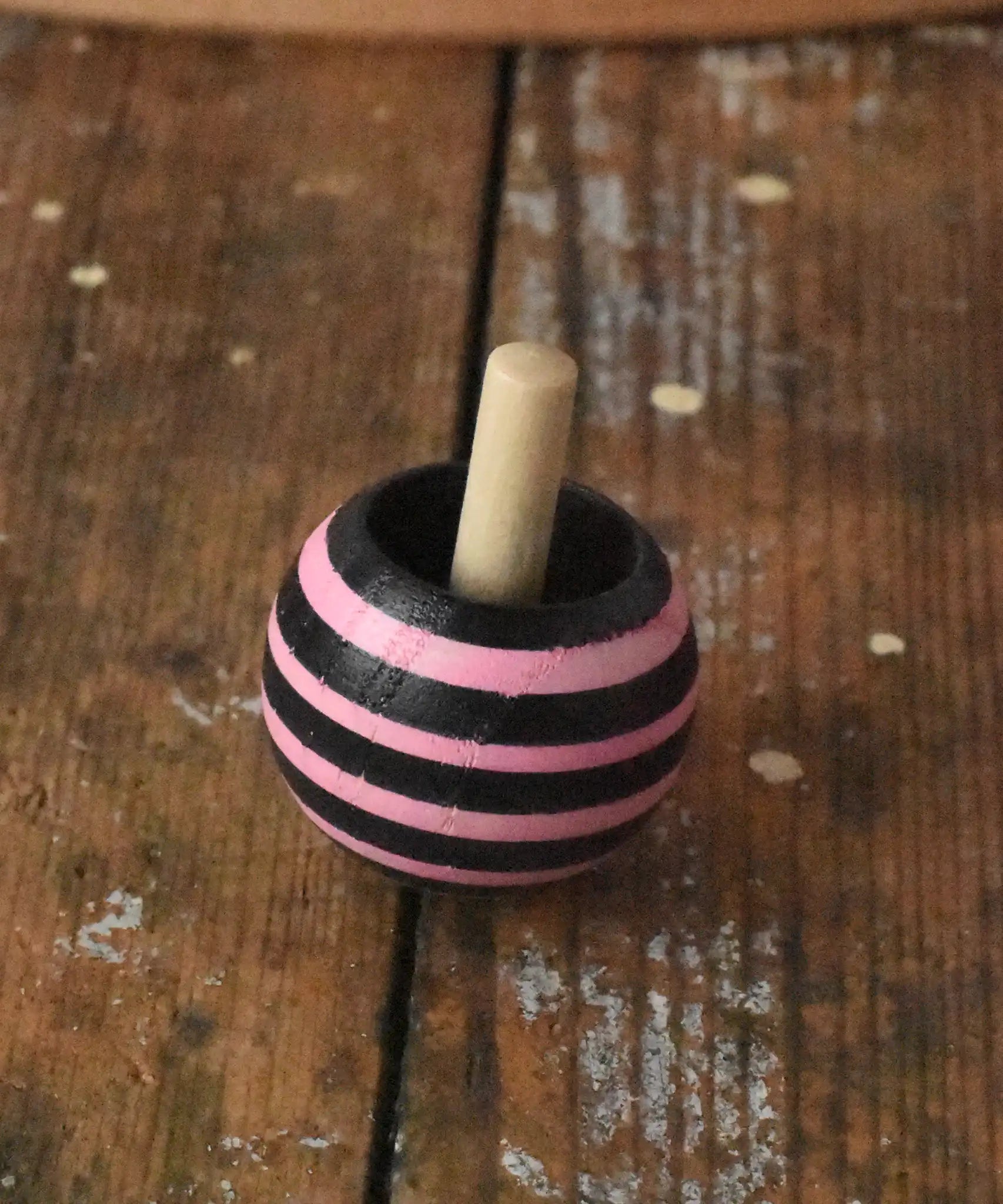 Pink striped Mader tango turn-over spinning top placed on a wooden desk in the Babipur playroom. 