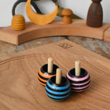 Three Mader tango turn-over spinning tops placed on an oak spinning plate on a wooden desk in the Babipur playroom. 