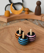 Three Mader tango turn-over spinning tops placed on an oak spinning plate on a wooden desk in the Babipur playroom. 