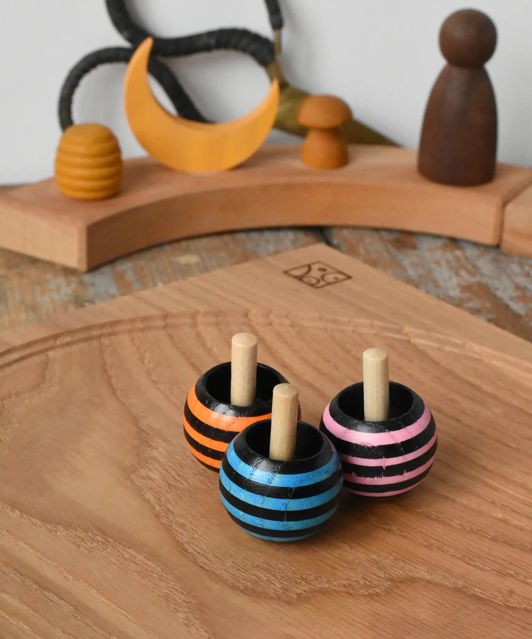 Three Mader tango turn-over spinning tops placed on an oak spinning plate on a wooden desk in the Babipur playroom. 