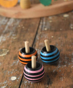 Three striped Mader tango turn-over spinning tops placed on a wooden desk in the Babipur playroom. 