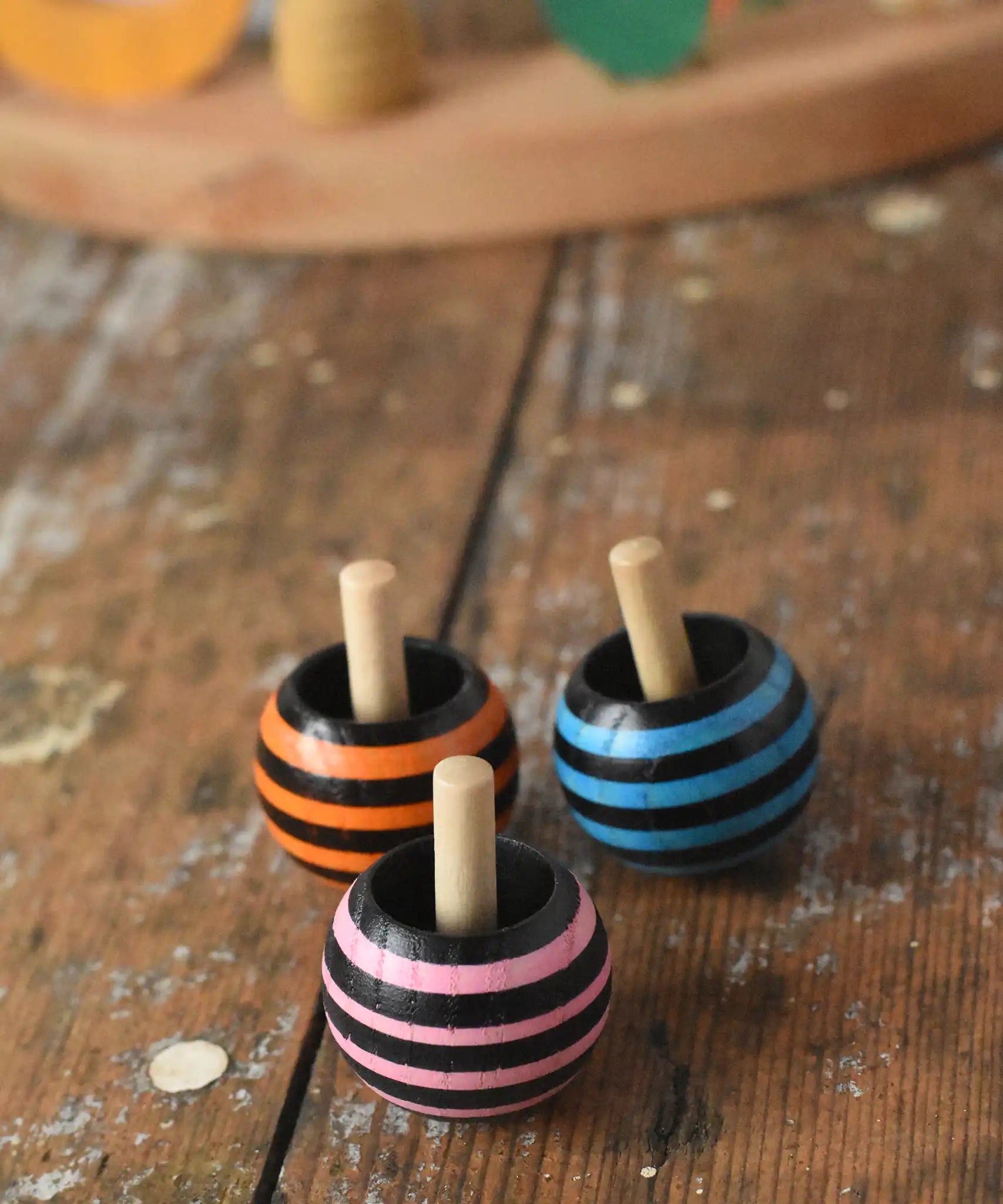 Three striped Mader tango turn-over spinning tops placed on a wooden desk in the Babipur playroom. 